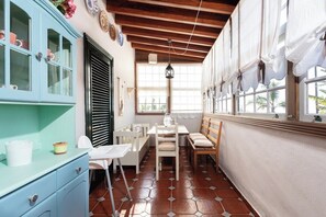 A narrow room with a dining table, chairs, a blue cabinet, and a window with curtains.