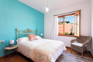 Un dormitorio con cama, una silla, un ventanal y vistas al exterior.