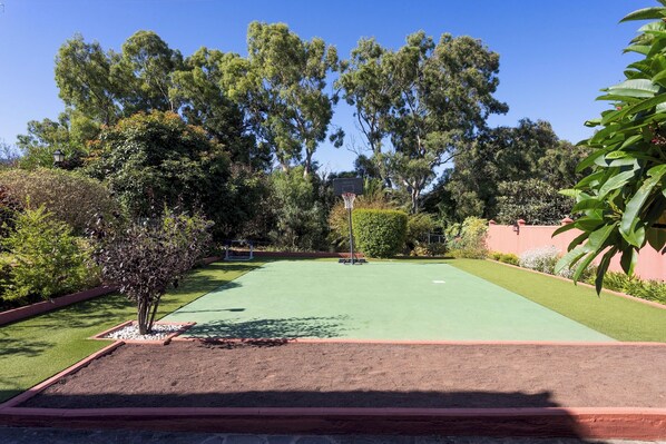 A well-maintained outdoor area with a green artificial turf surface, surrounded by various trees and shrubs.