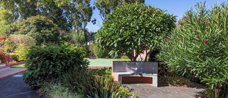 Un chemin pavé agrémenté d’un banc, entouré de différentes plantes et arbres.
