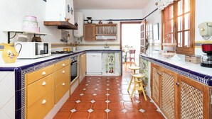 Une cuisine avec un sol carrelé, des meubles de rangement en bois, un four à micro-ondes et un évier.