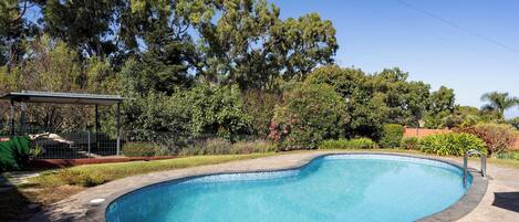 A swimming pool with a stone border, surrounded by trees and a fenced area.