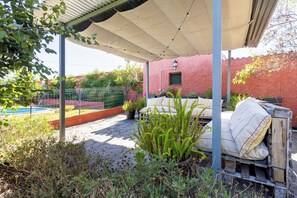 Un espacio exterior techado con piscina, plantas en macetas y zona de estar con cojines.