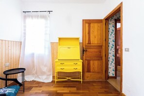 A room with a wooden door, a yellow dresser, a black chair, and a white curtain.