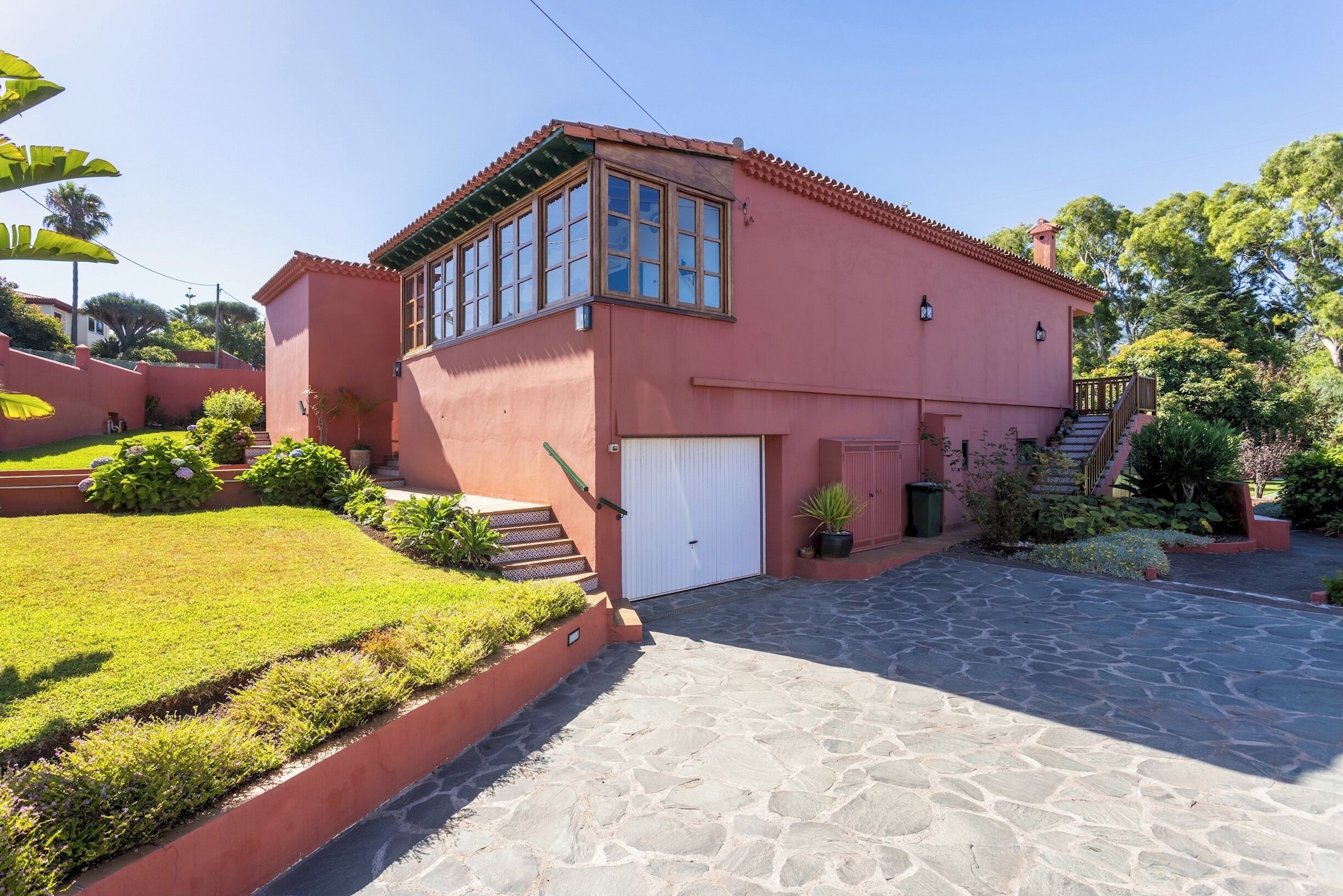 Una casa de dos pisos con fachada roja, puerta de garaje blanca y entrada de adoquines.