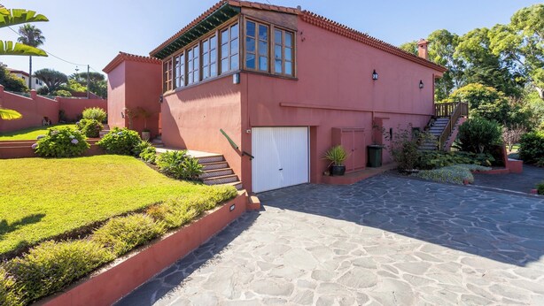 Une maison à deux étages avec une façade rouge, une porte de garage blanche et une allée pavée de pierres.