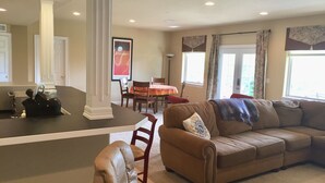 A spacious living room with a brown sofa, a dining table, and a kitchen area with a black countertop. - Spread out in a large,1600 sq foot comfort suite 1 bedroom plus additional nook (Longmont)