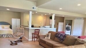 A living room with a sofa, a rocking chair, a dining area with a bar, a kitchen, and a laundry room. - Spread out in a large,1600 sq foot comfort suite 1 bedroom plus additional nook (Longmont)