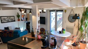 A modern kitchen with a central island, a dining area with a round table, and a living space with a sofa and artwork. - Maisonette with terrace 5 minutes from the beaches (Anglet)