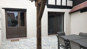 Eine Terrasse mit Tisch und Stühlen, ein Holzmast und eine Tür mit Fensterglas.