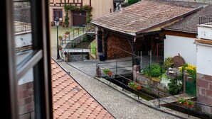 Blick durch ein Fenster auf eine Stadt mit traditioneller Architektur, darunter ein Kirchturm und eine schmale Straße mit Häusern.