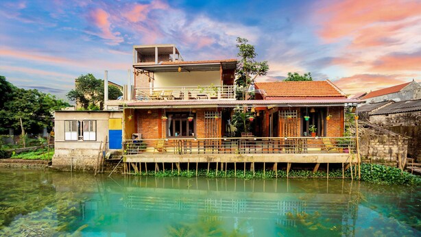 A houseboat with a balcony, a small attached structure, and a dock extending into a clear water body with aquatic plants. - Tam coc Paradise Homestay (Nam Hoa Lu)