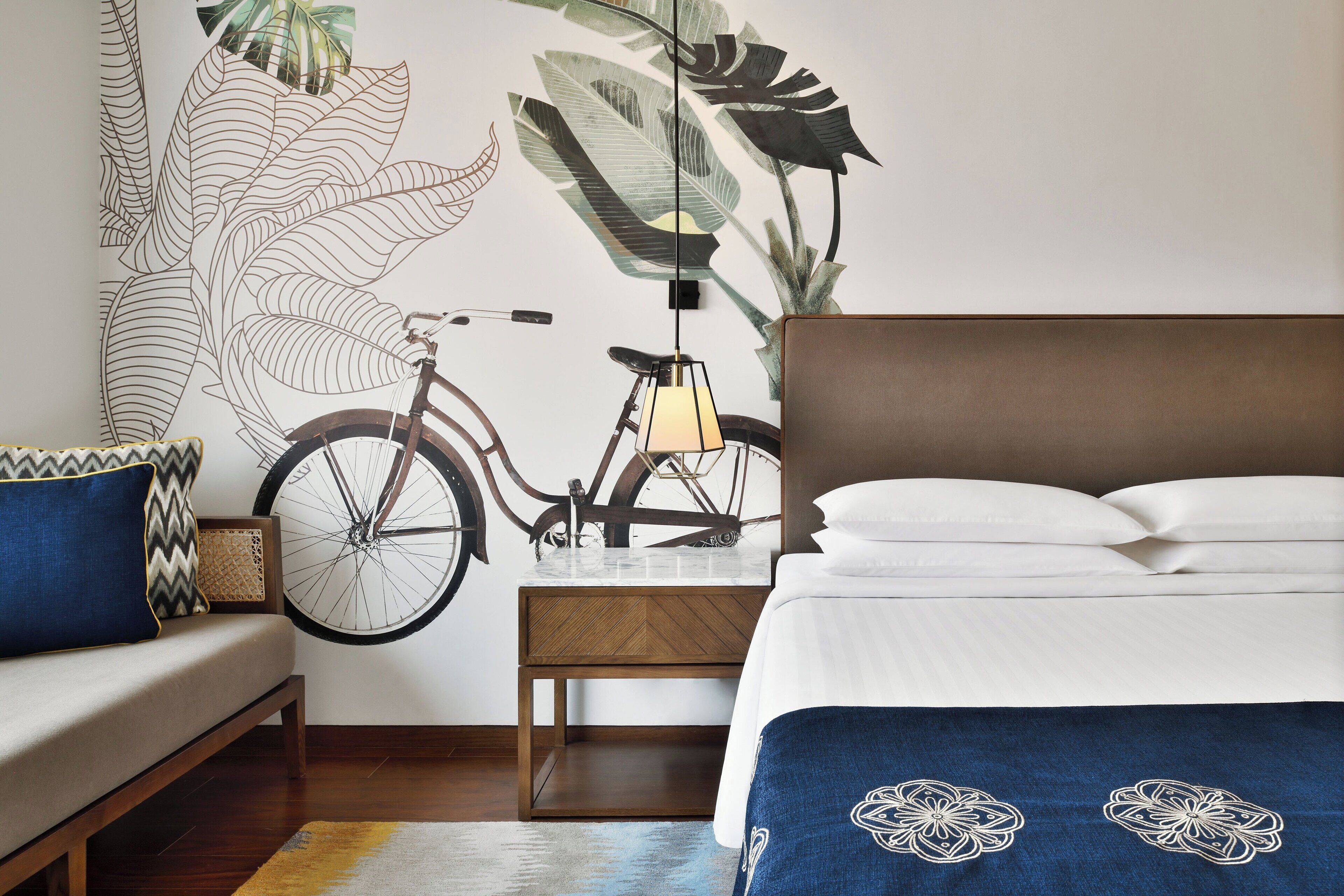 Een slaapkamer met een bed, een houten nachtkastje, een fiets en een muurschildering.