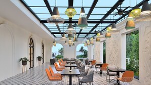 A restaurant with a long table layout, hanging pendant lights, and a patterned floor. - Port Muziris, a Tribute Portfolio Hotel by Marriott, Kochi Airport (Aluva)