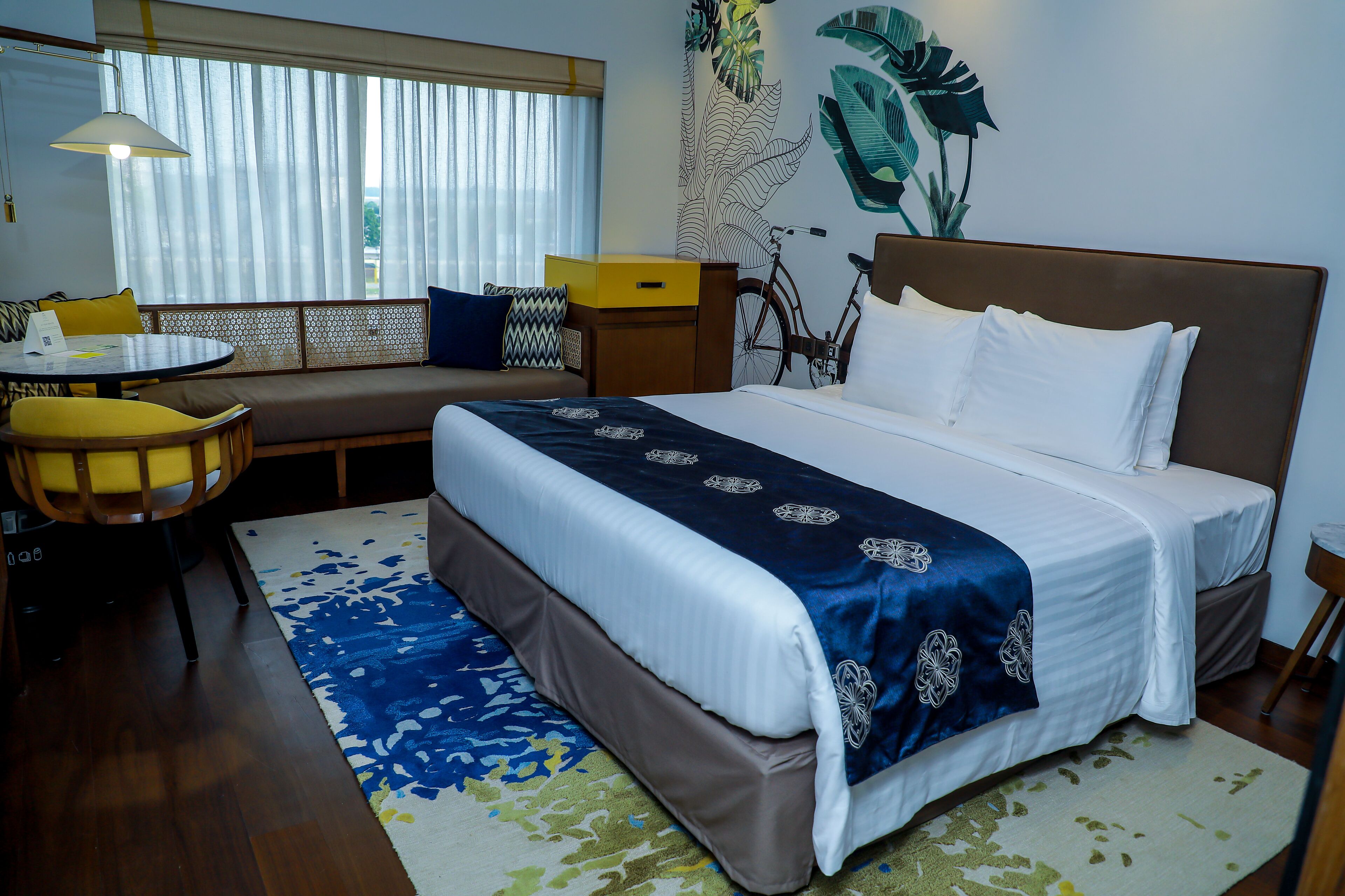 A hotel room with a bed, a sofa, a dining table, and a bicycle.