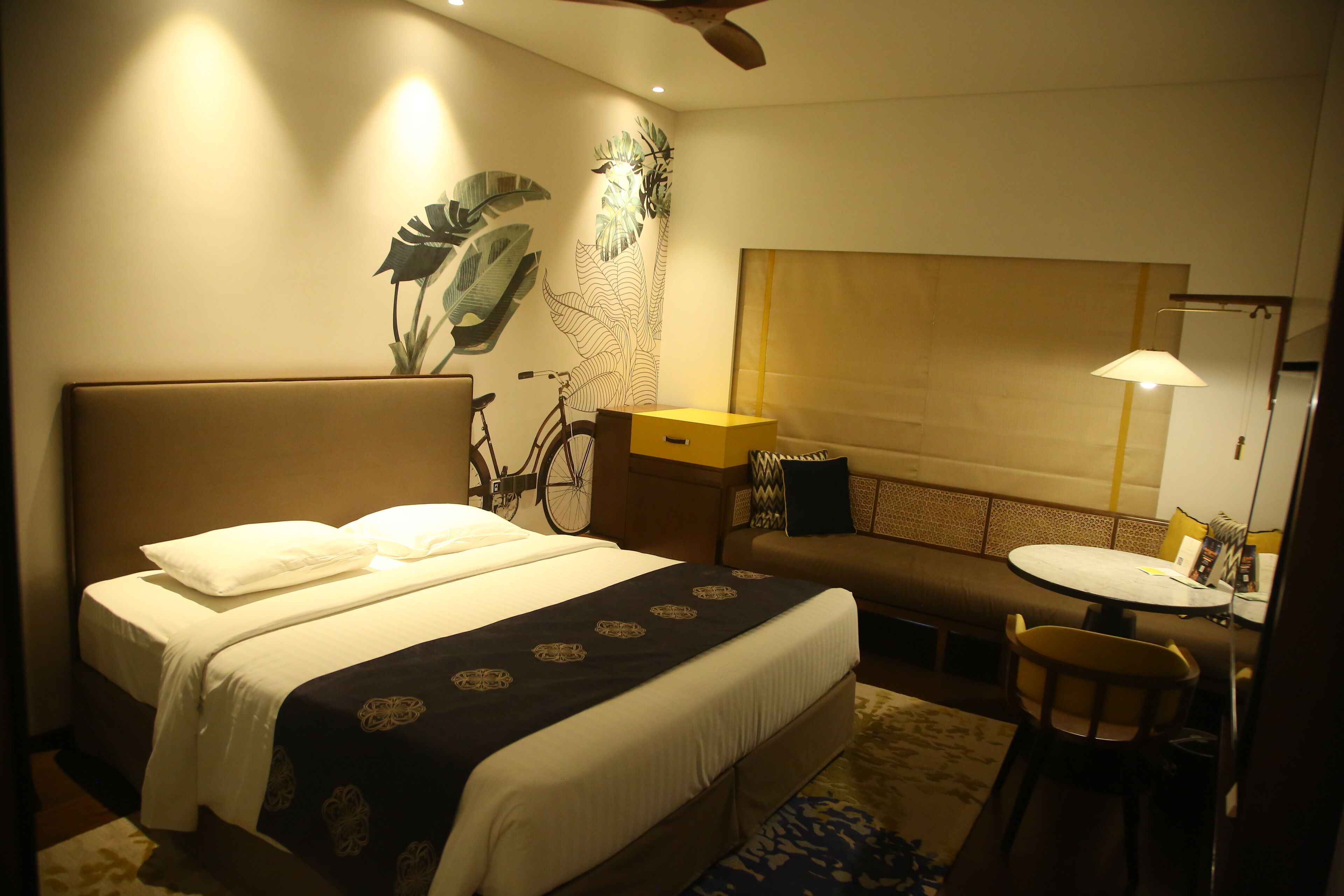 A hotel room with a bed, a bicycle, a round table, and a chair.