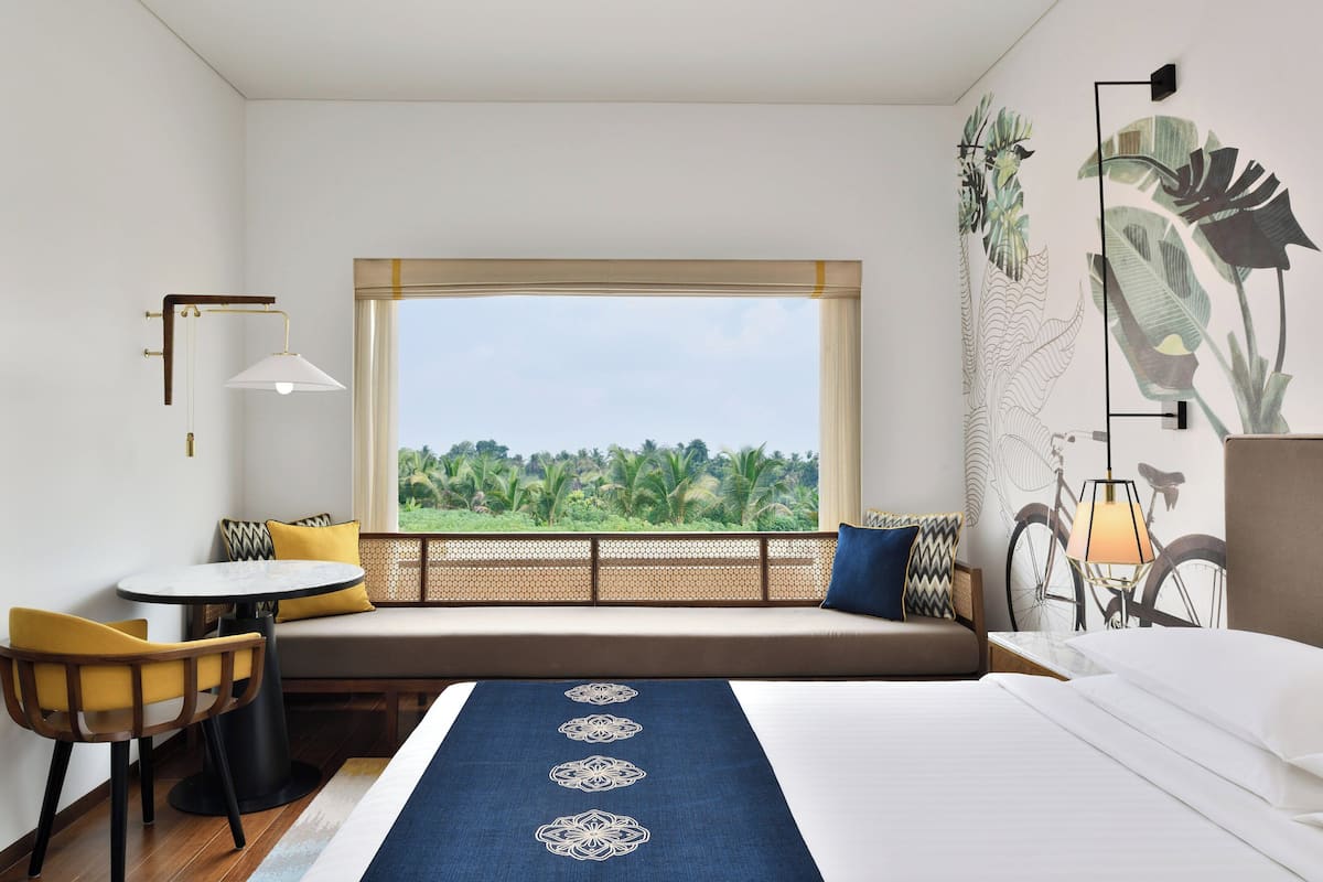 A hotel room with a large window, a bed, a sofa, a small table, and a chair.