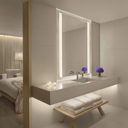 A modern bathroom with a large mirror, a sink, and a bench.