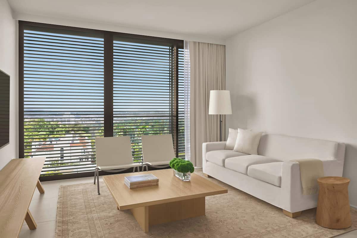 Een moderne hotelkamer met een groot raam, een witte bank, een houten salontafel en een bijzettafeltje.