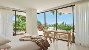 Une chambre moderne avec un grand lit, un coin repas comprenant une table et des chaises, et un balcon offrant une vue sur la verdure et les bâtiments.