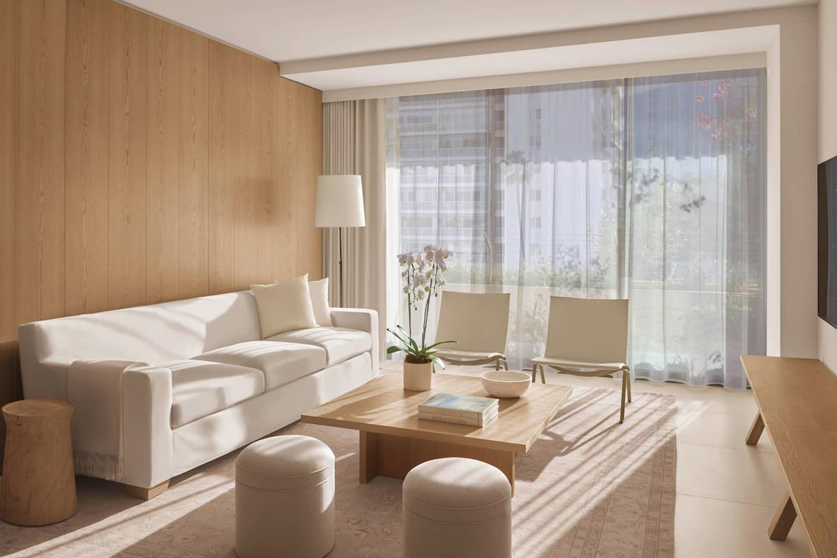 Een moderne woonkamer met een witte bank, een houten salontafel en een groot raam met transparante gordijnen.