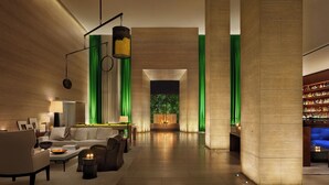 Un hall d’entrée spacieux au design moderne, comprenant un coin salon avec des canapés et une table basse, un bar bien garni et une grande fenêtre ornée de rideaux verts.