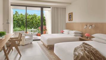 A hotel room with two beds, a desk, chairs, a balcony with a view of greenery and flowers, and a wooden headboard.