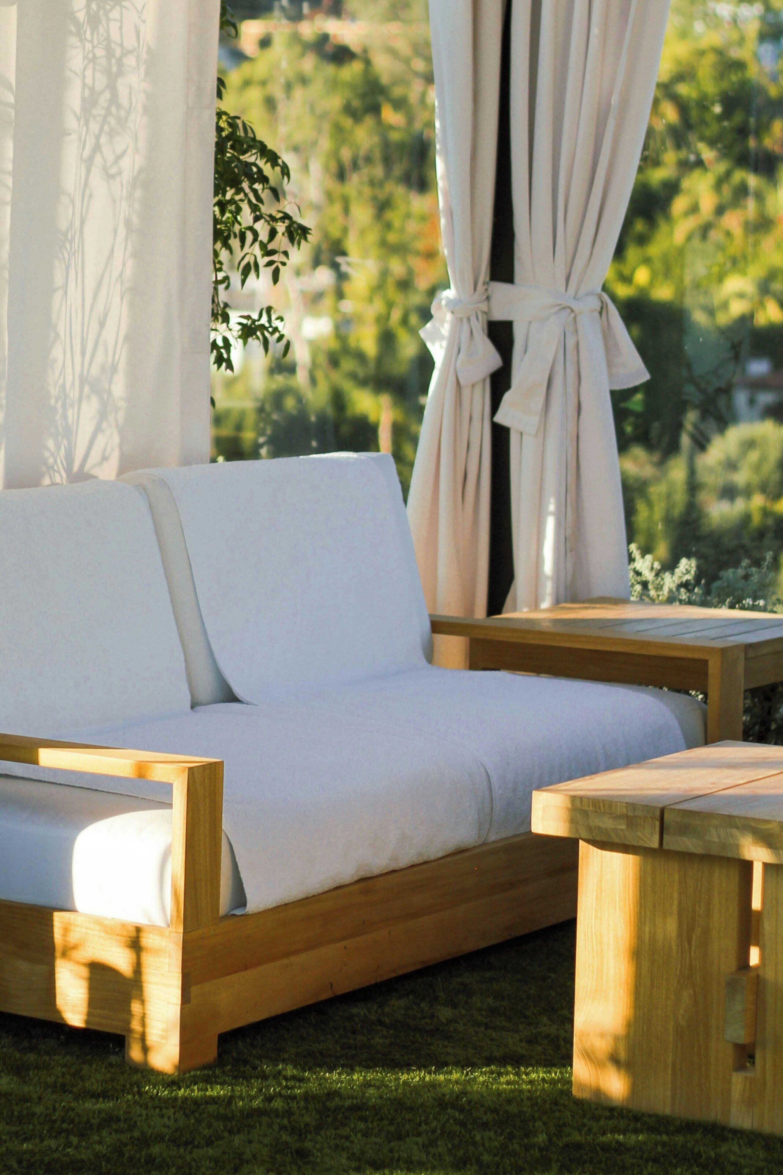 A wooden sofa with white cushions in a garden setting.