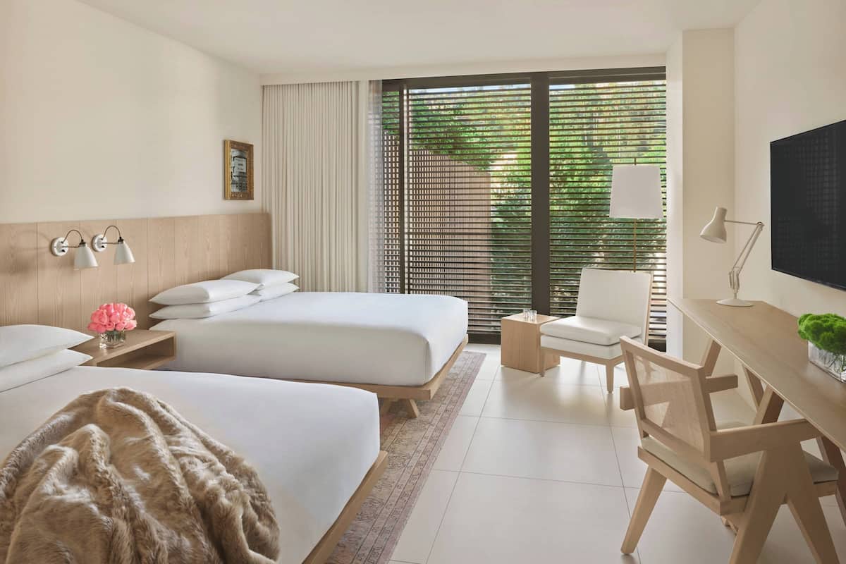 Een hotelkamer met twee bedden, een bureau, een stoel, een televisie en een raam met jaloezieën.