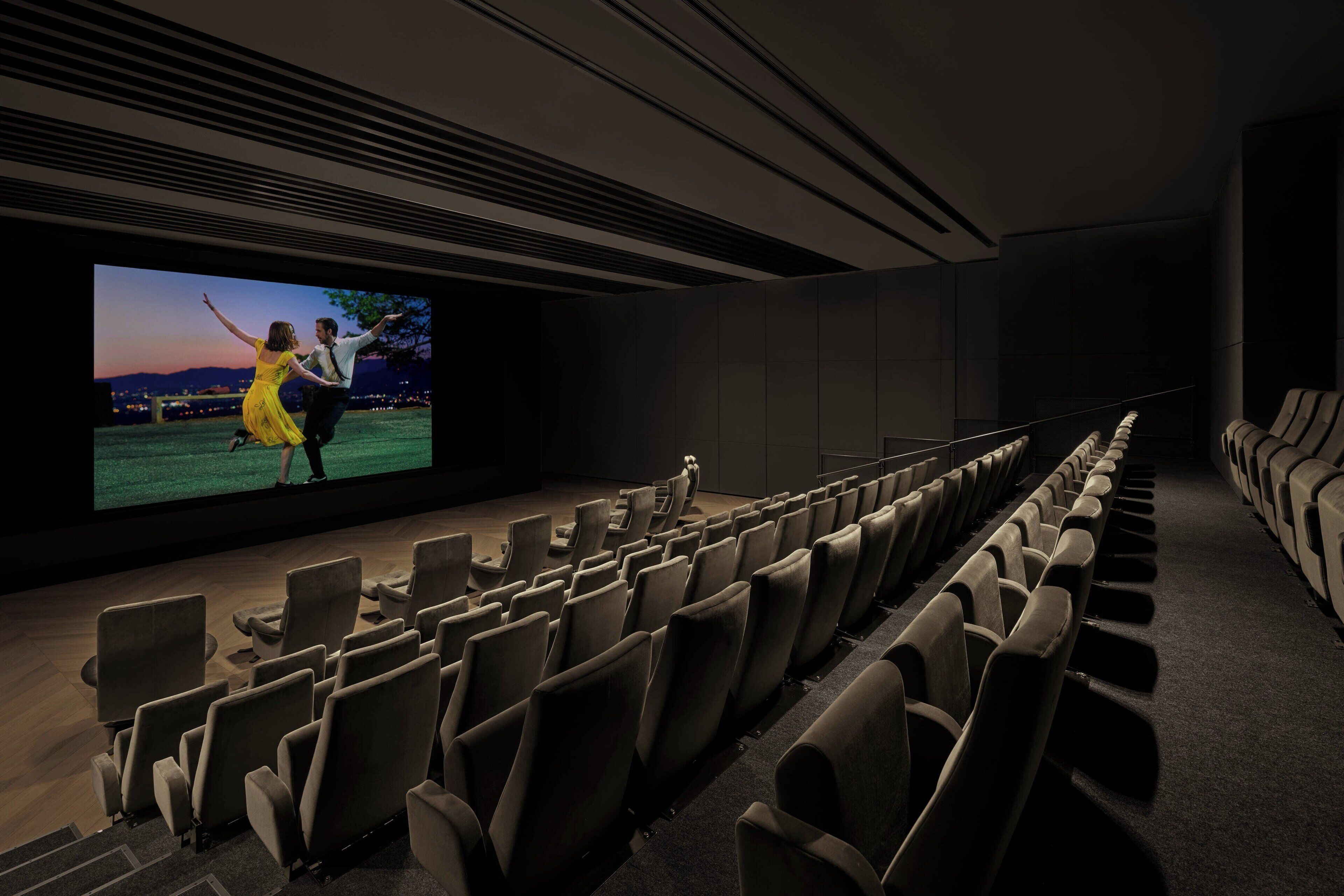 An empty movie theater with rows of seats and a large screen displaying a film.