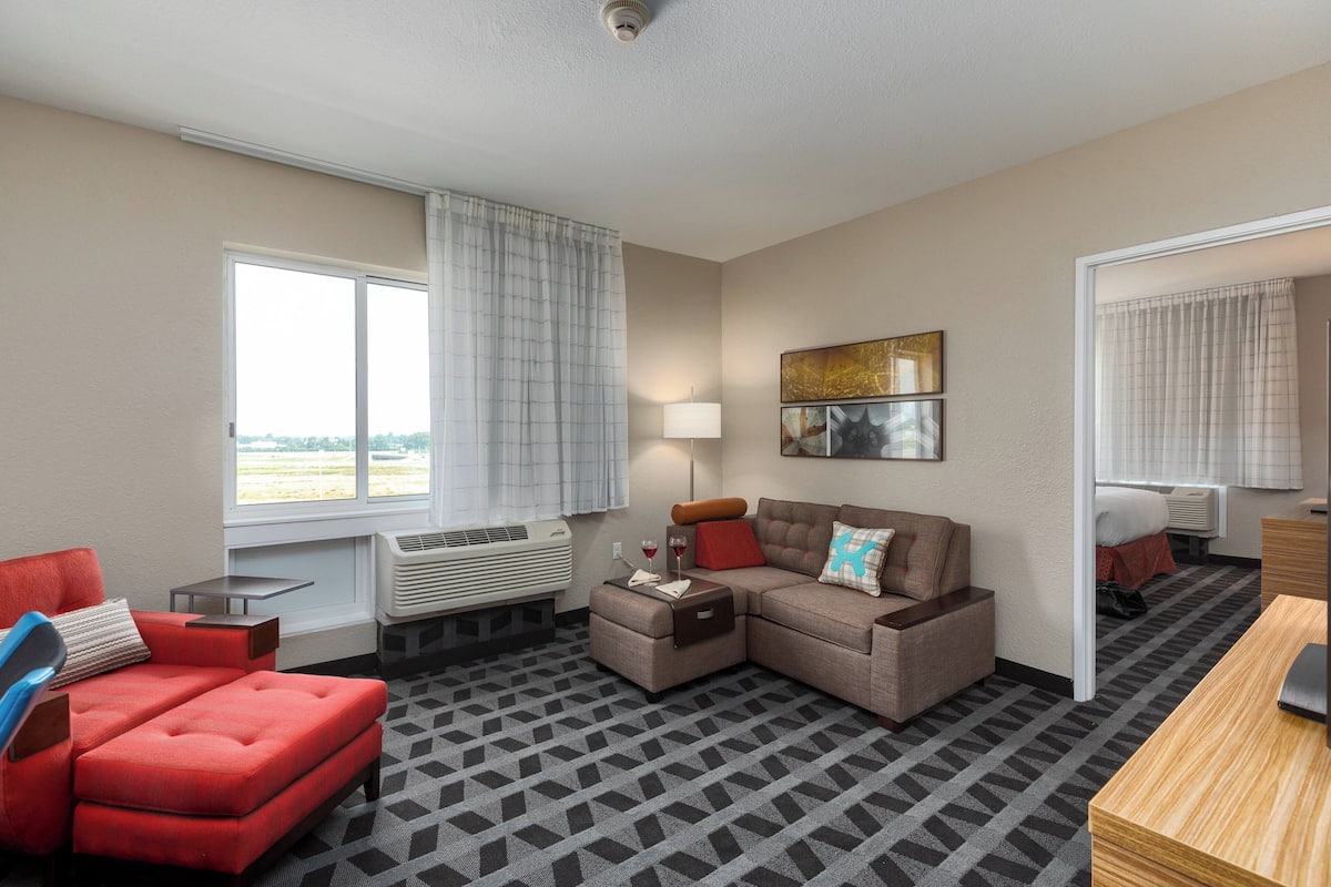 Una habitación de hotel con un sofá modular, un sillón rojo, una mesita y un escritorio.