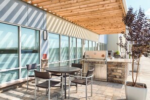 Un patio exterior con una parrilla, asientos y vistas a la calle.