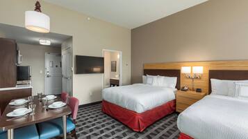 Une chambre d’hôtel comprenant un coin repas, deux lits avec des couvre-lits rouges, une tête de lit en bois, un téléviseur à écran plat et un bureau avec des chaises.