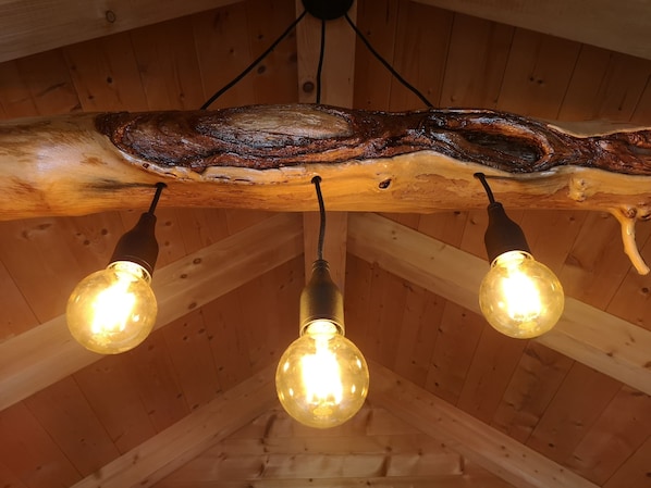 Un plafond en bois rustique, agrémenté de trois lampes à ampoules apparentes suspendues à une structure évoquant une branche d’arbre.