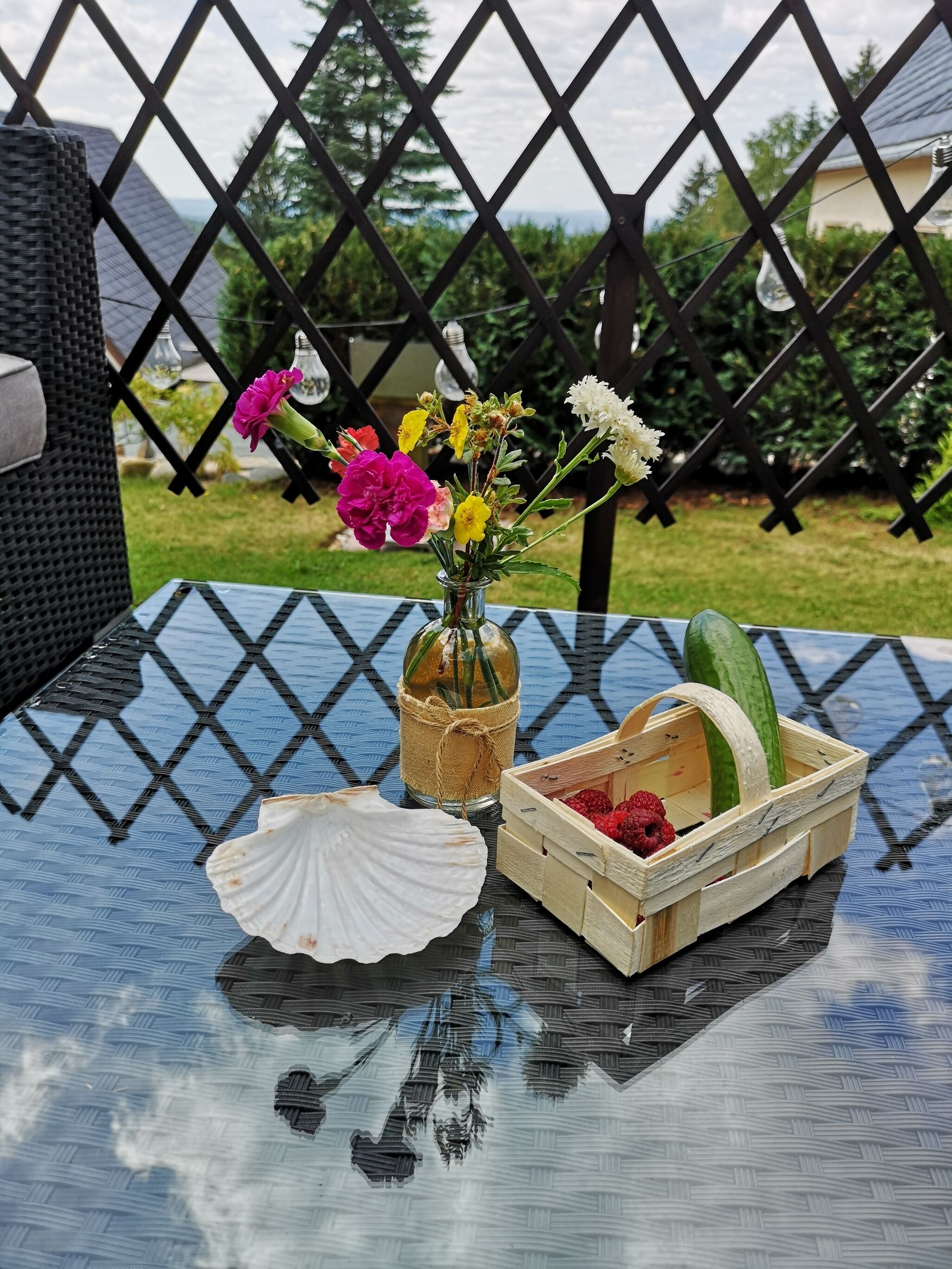 Uma mesa de vidro com um vaso de flores, uma cesta de madeira com framboesas e uma concha.