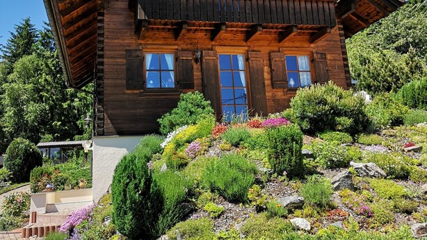 Un chalet en bois doté d’un balcon, entouré d’un jardin aménagé avec différentes plantes et fleurs.