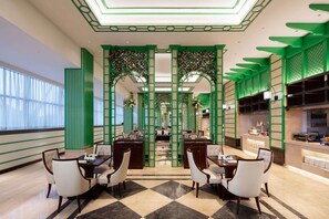 A hotel lobby with a checkered floor, green decorative columns, and a reception desk.