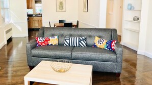 Ein graues Sofa mit bunten Kissen, ein Holztisch und eine Küche im Hintergrund.