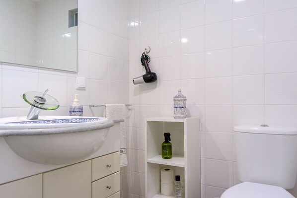 A bathroom with a white sink, toilet, and shelves with toiletries.
