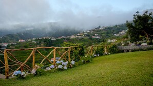 A rural landscape with a vineyard, a stone wall, and houses on a hill in the background. - Recanto das Florenças (2) – Great Views & Sunsets (Arco Da Calheta)