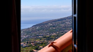 A view from a window overlooking a hillside with houses and a coastline. - Recanto das Florenças (2) – Great Views & Sunsets (Arco Da Calheta)