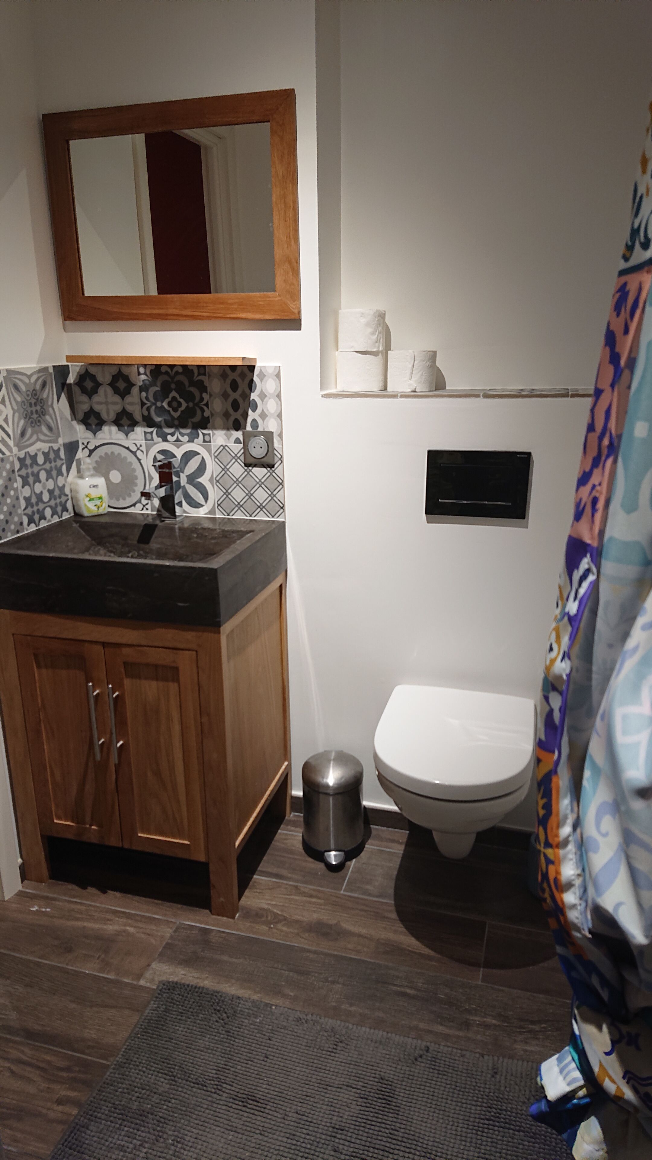 Un baño con un armario de madera, un lavamanos, un inodoro y un cubo de basura.