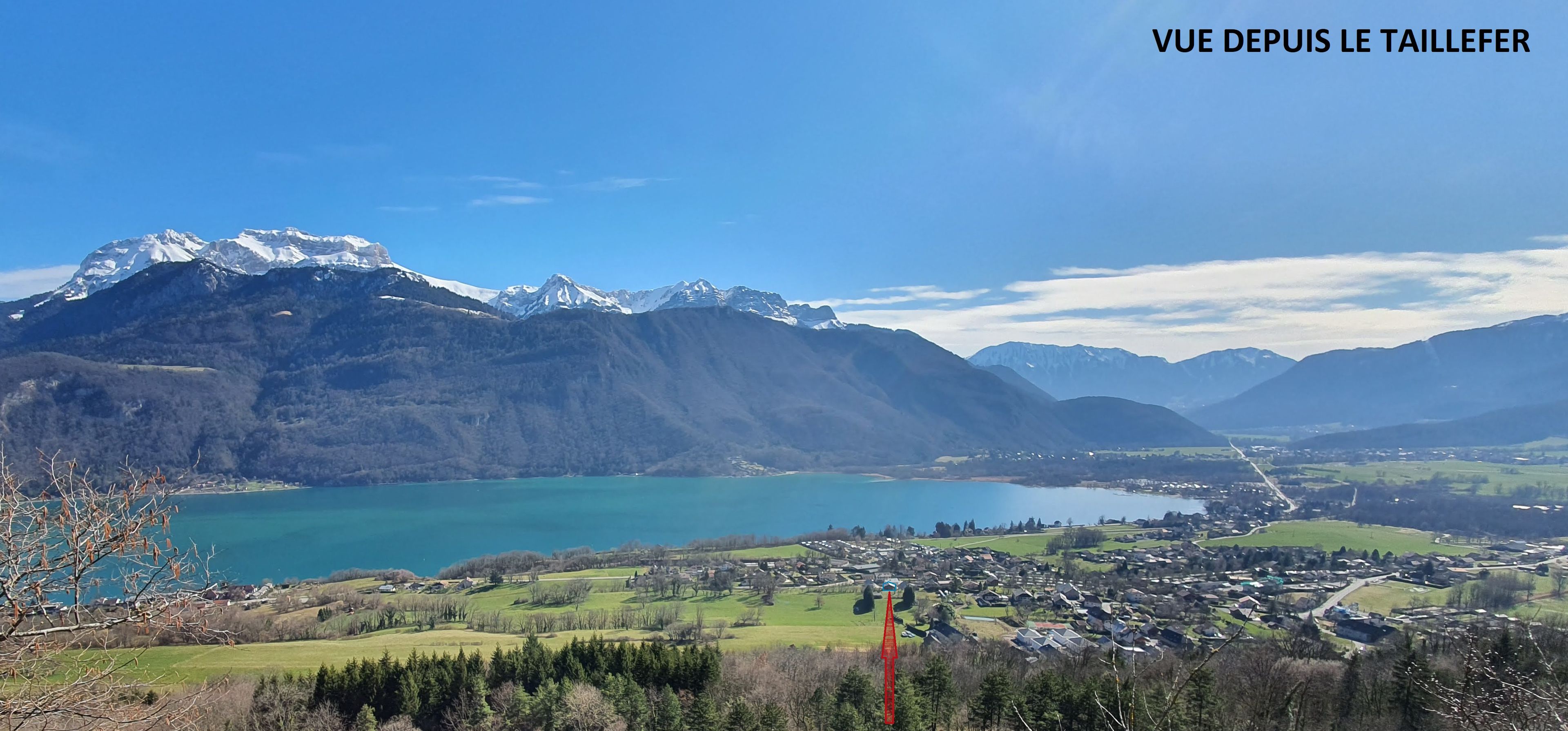 A scenic view of a mountainous landscape with a lake, a small town, and a red tower.