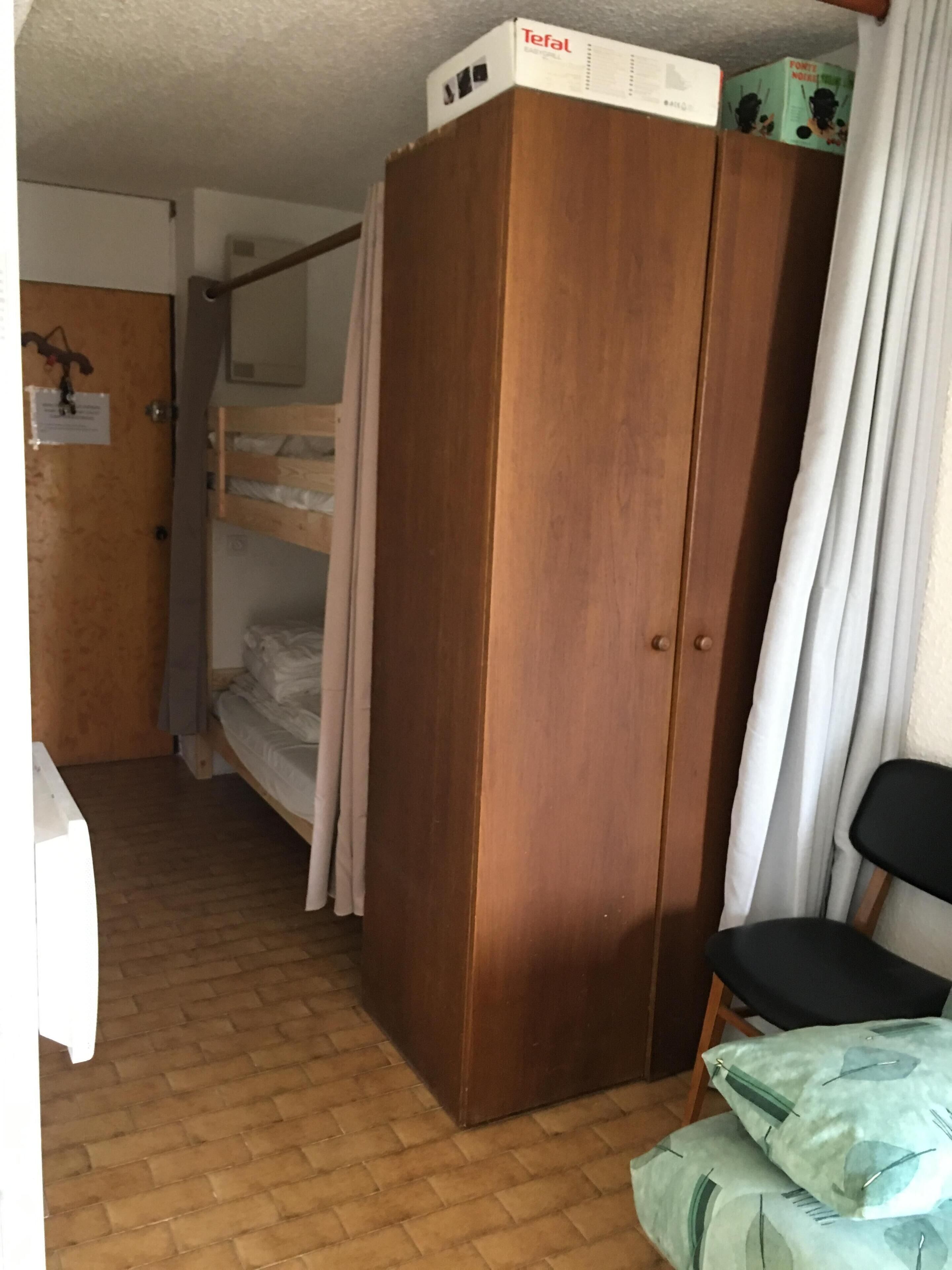 Una stanza con un'armadiatura in legno, un letto a castello, una sedia e un tavolino.