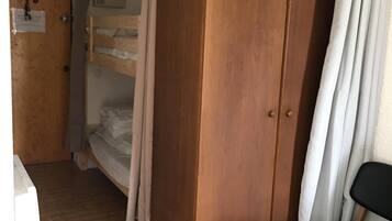 Una stanza con un'armadiatura in legno, un letto a castello, una sedia e un tavolino.