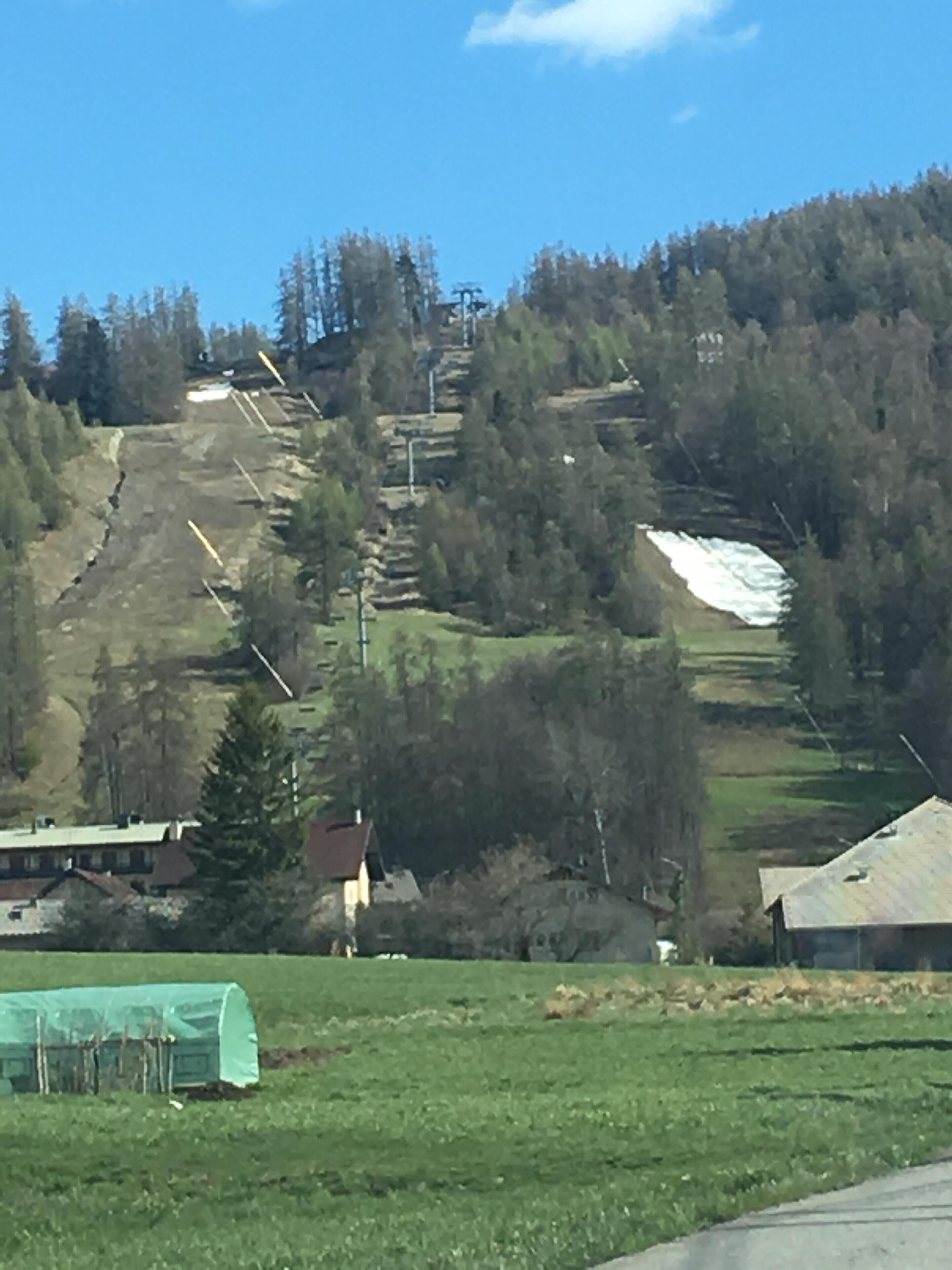 Un paysage rural avec une colline, une serre et quelques bâtiments.