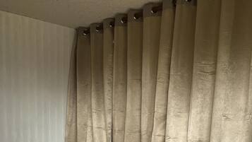 Una cama con colchón blanco y detalles negros, ubicada bajo cortinas color beige.