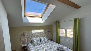 A bedroom with a skylight, a bed with a patterned bedspread, a radiator, and a window with curtains.