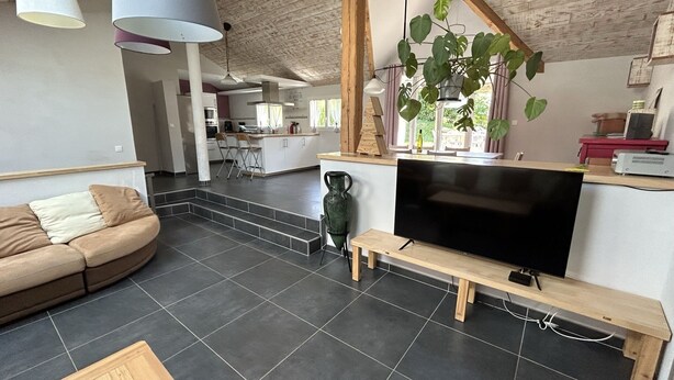 A spacious living area with a large TV, a sofa, a bench, and a dining table.