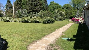 Ein gepflasterter Weg in einem gepflegten Grünbereich mit üppiger Vegetation und blühenden Pflanzen im Hintergrund.